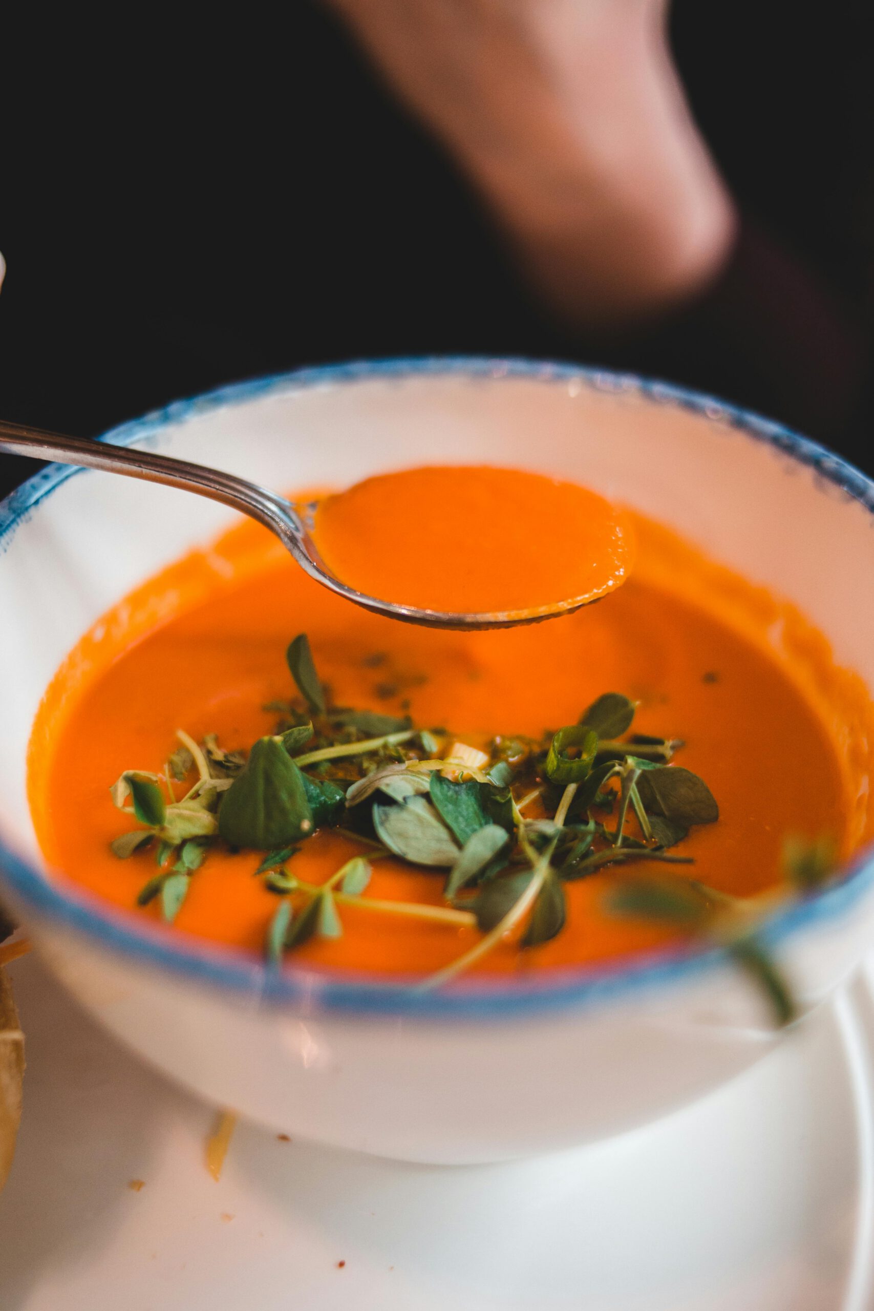 Tomatensoep met kruiden erop en een lepel erboven.